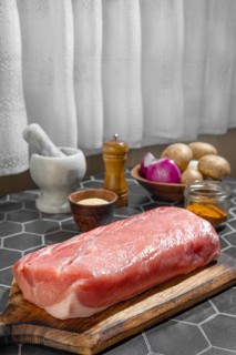 Whole uncut raw pork tenderloin on kitchen table with spice and mushrooms