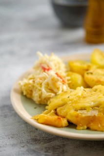 Close-up view of baked pork fillet with melted cheese served with fried potato and cabbage salad