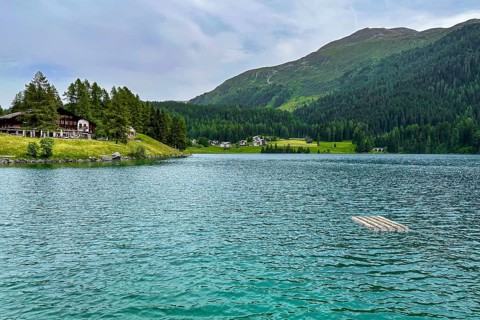 Mountain lake with clear blue water, surrounded by green forests and meadows with scattered houses,