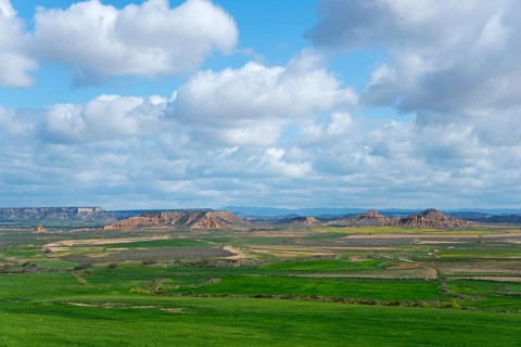 Vast landscape with green fields and hills under a cloudy sky, peaceful atmosphere, Bardenas Reales