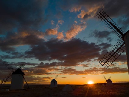 Several windmills in front of a dramatic sunset with colourful sky and clouds, creating a calm and