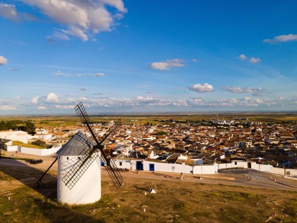 Windmill overlooking a Spanish town, nestled in a vast landscape under a clear blue sky with a few