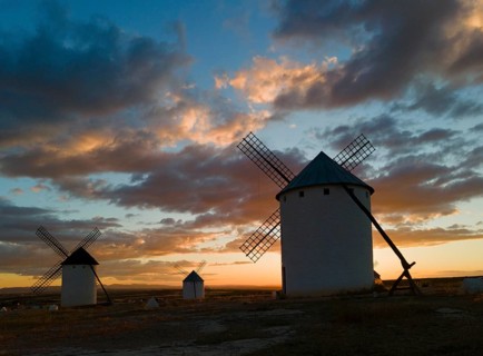 Three windmills in front of a dramatic sunset with a colourful sky and clouds. The silhouettes of