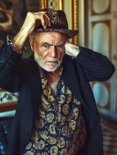 Elderly man wearing a leopard hat and patterned shirt looks thoughtful in a vintage setting, AI