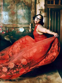 Woman in a flowing red dress with floral patterns, in an ornate and luxurious room featuring a