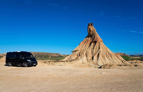 Motorhome in a barren desert landscape with striking rock formations and a clear blue sky,