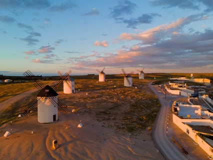 Landscape at sunset with windmills and a road leading to an illuminated village, aerial view,