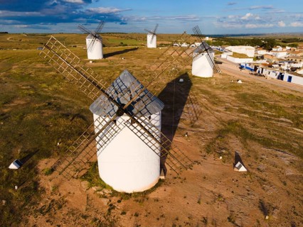 Close-up of several windmills in a green landscape under a blue sky with clouds, aerial view,