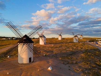 Several windmills are scattered in a wide landscape under a slightly cloudy sky, aerial view,