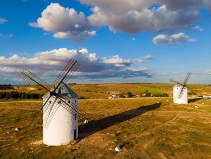 Two windmills stand in a wide landscape under a partly cloudy blue sky, aerial view, windmills,