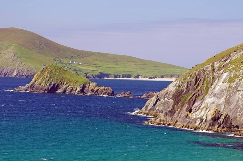 Dramatic coastline with high green cliffs and blue ocean waters under clear skies, Slea Head Drive,