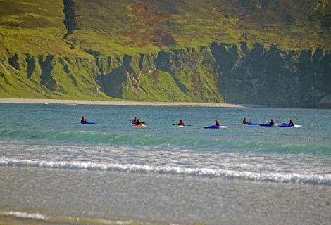 Group of surfers on their boards on the sea near rocky shore, Achill Island, County Mayo, Ireland,