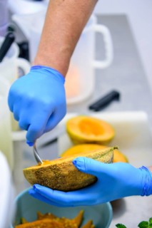 Person scooping cantaloupe with a spoon in the kitchen, emphasizing food preparation, hand hygiene,