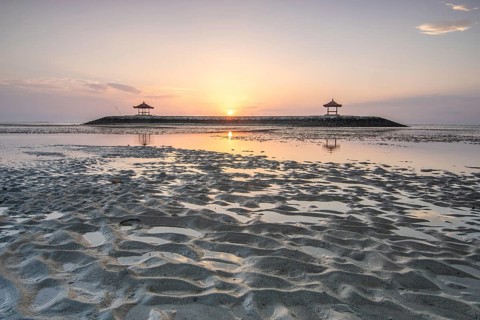 Fantastic sunrise on the beach with small temples. View of the sea as far as the horizon. Sanur,