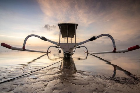 Fantastic sunrise on the beach with small temples and a traditional fishing boat, Jukung. View of