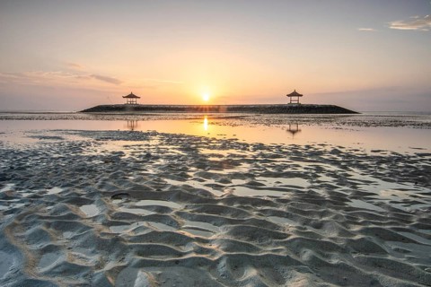 Fantastic sunrise on the beach with small temples. View of the sea as far as the horizon. Sanur,