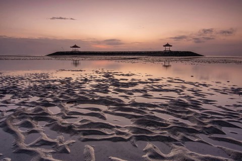 Fantastic sunrise on the beach with small temples. View of the sea as far as the horizon. Sanur,