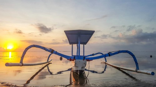 Fantastic sunrise on the beach with small temples and a traditional fishing boat, Jukung. View of
