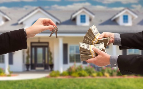 Real estate agent handing over house keys for stacks of money in front of new house