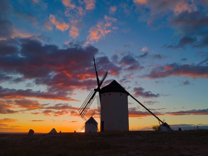 Windmills at dusk, silhouettes of buildings stand out against the colourful sky and scattered
