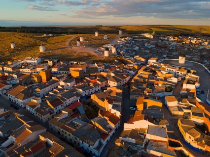 Roofs and houses of a village at dusk with windmills in the background and orange lighting, aerial