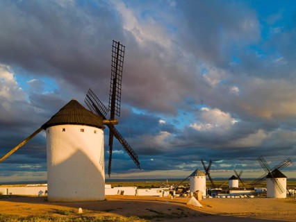White windmills in an open landscape with dramatic clouds and sunbeams in the background,