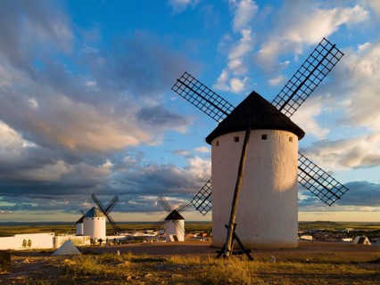 Several windmills in an open landscape, illuminated by sunlight, under a cloudy sky, windmills,