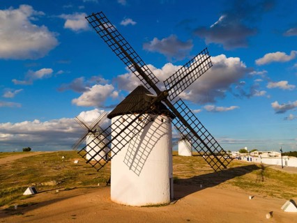 White windmills in the sun under a blue sky with clouds, surrounded by an open landscape, aerial