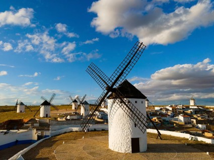 White windmills stand under a partly cloudy blue sky, with a village in the background, aerial