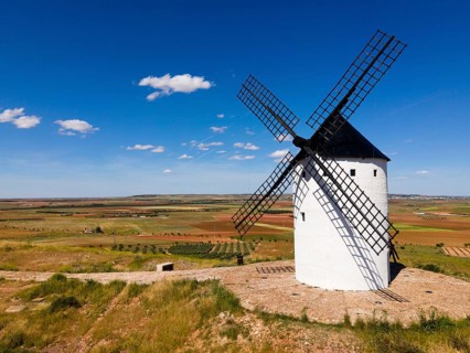 A single white windmill stands on a grassy field under a blue sky with few clouds, aerial view,