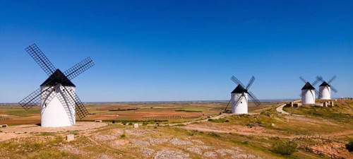 Several white windmills spread across a vast agricultural area under a clear blue sky, aerial view,