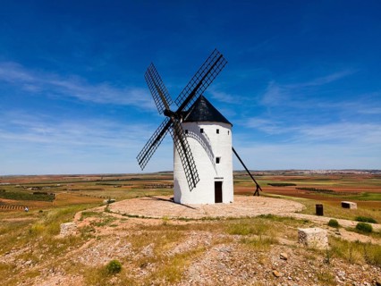 A lone white windmill stands in a field under a bright blue sky, aerial view, Alcazar de San Juan,