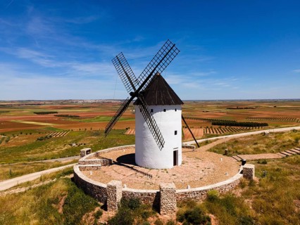 White windmill with black roof on a hill surrounded by stone walls and wide fields, aerial view,