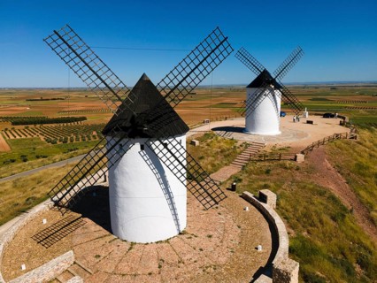 Two white windmills with black roofs in a wide field landscape in sunny weather, aerial view,