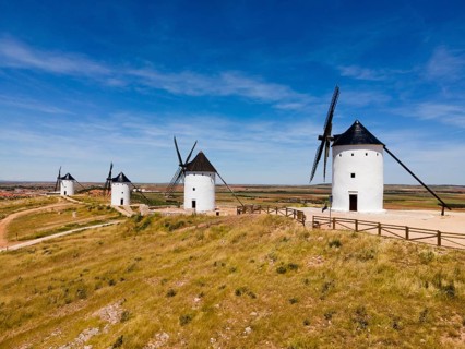 Several white windmills with black roofs in a vast scenic landscape under a clear blue sky, aerial