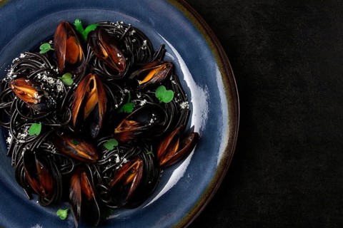 Spaghetti with black squid, black pasta, with boiled mussels, on a black plate, with parsley and