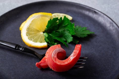 Chum salmon, cold smoked, on a fork, with lemon and parsley, top view, close-up, no people