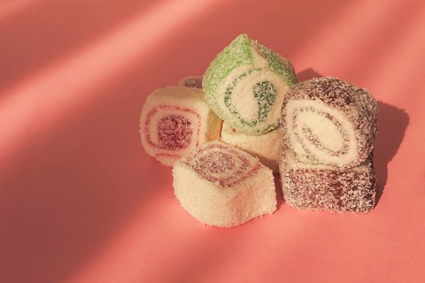 Traditional Turkish delight, rols shape, in coconut flakes, on pink background, sunlight,
