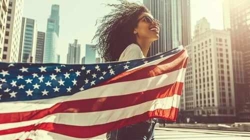 Happy woman holding an American flag in a city with tall skyscrapers on a windy day, AI generated