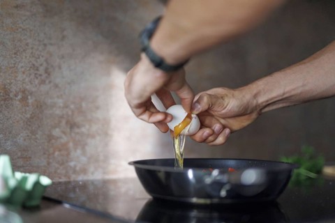 Cooking topic. A man cracks a raw egg into a pan. Berlin, 01.08.2024