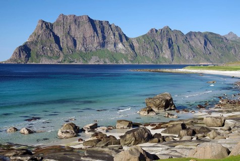 Beach with clear blue water and rocks, while impressive mountains form the background, Uttakleiv