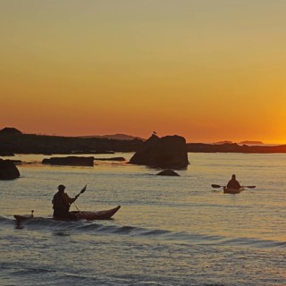 Two people kayaking on a calm water at sunset, Ramberg, Flakstad, Flakstadoya, Lofoten, Nordland,