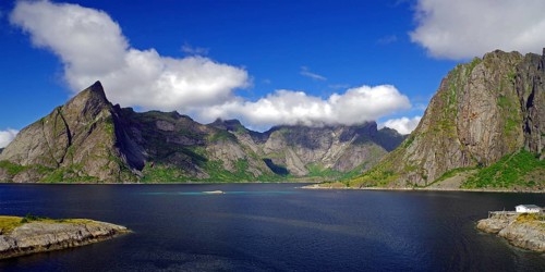 Impressive mountains under a blue sky with white clouds next to a calm fjord, Reinefjord, Hamnoy,