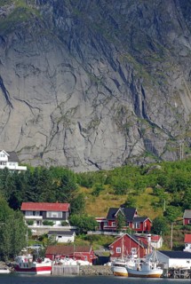 Idyllic fishing village with red house and fishing boats in front of an impressive rock face,