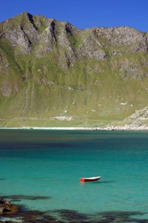 A red boat floats in a turquoise-coloured lake in front of a mountainous landscape, Haukland,