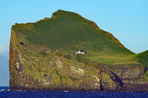 A small hut stands on a high, grassy cliff in the sea, Westman Islands, Iceland, Europe
