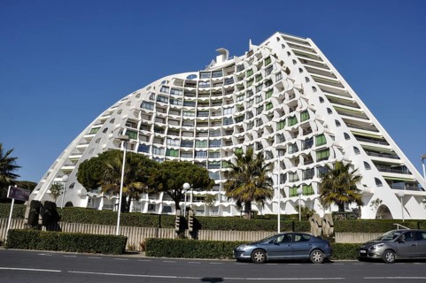 A modern curved building with a white facade and numerous balconies, set in an urban environment