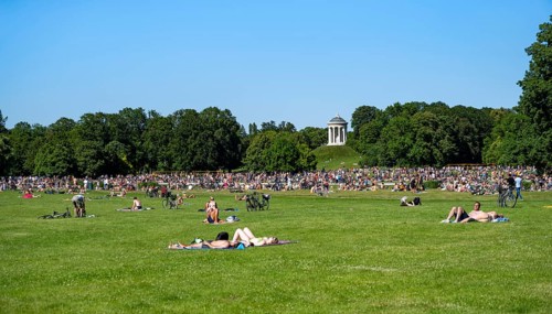 Many people in a meadow in the English Garden, people enjoying the summer day in the park behind