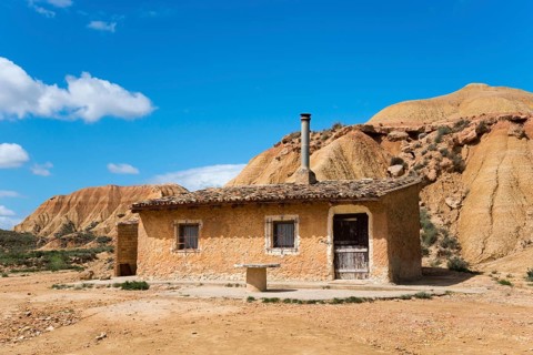 A small house stands in a dry, rocky landscape under a blue sky, Bardenas Reales Natural Park,