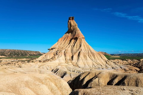 An impressive rock formation rises up in the desert-like landscape under a clear blue sky,